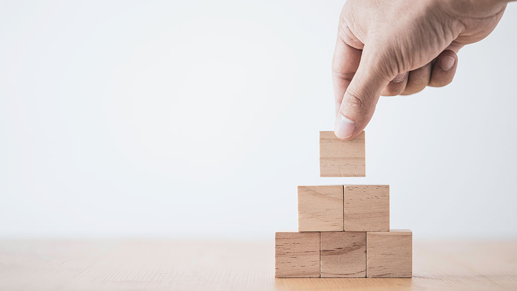 A hand building a pyramid from wooden building blocks